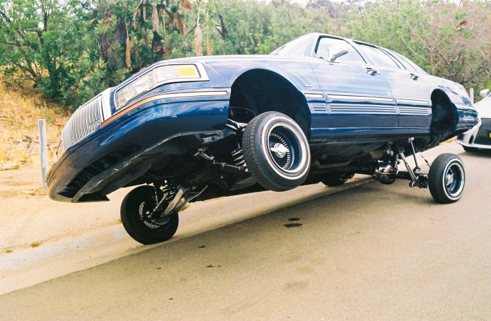 A blue lowrider with one wheel up in the air.