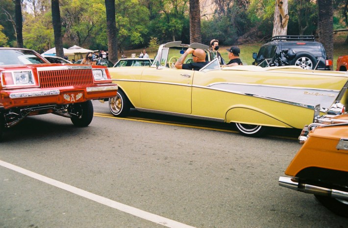 A red lowrider and yellow lowrider cruise by each other.