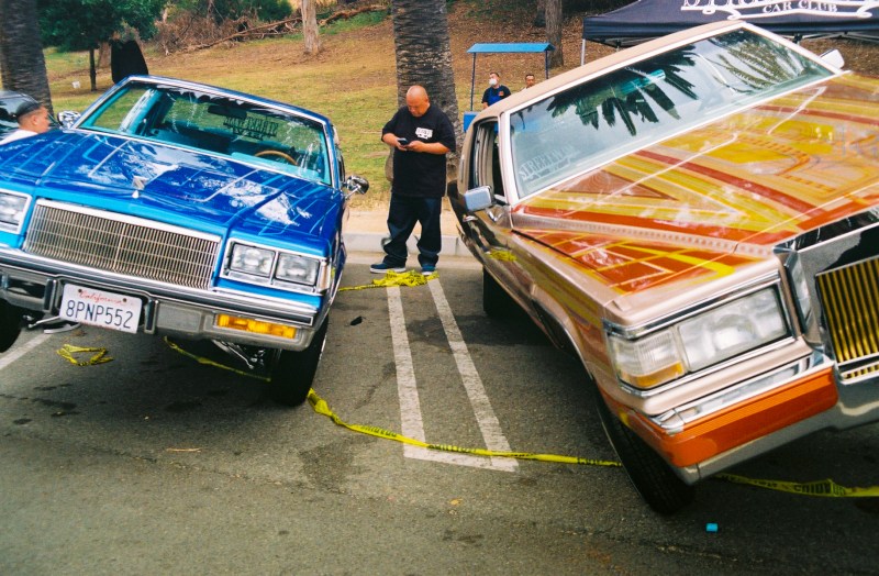 A blue lowrider parked next to an orange one, both hitting switches.