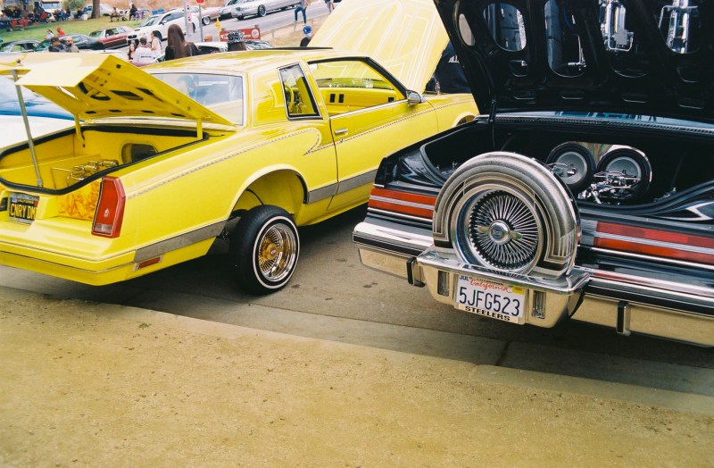 A yellow lowrider parked next to a dark blue one.
