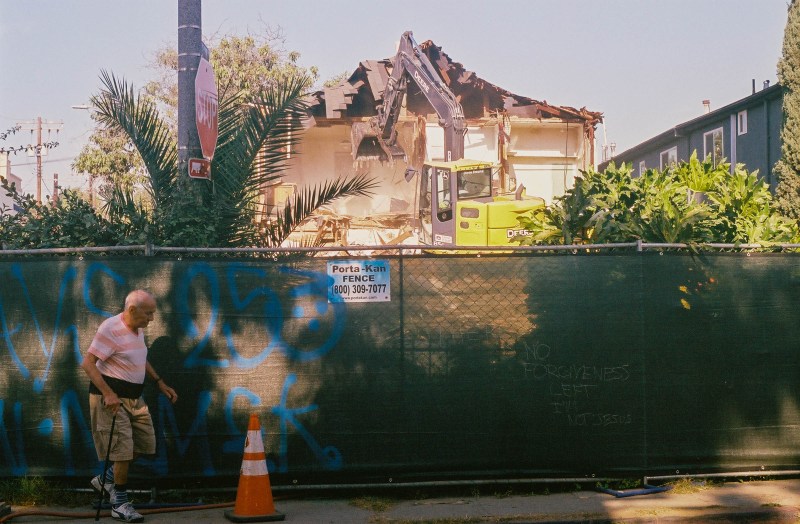 An elderly man walks by an 20th century craftsman house as it's being demolished.