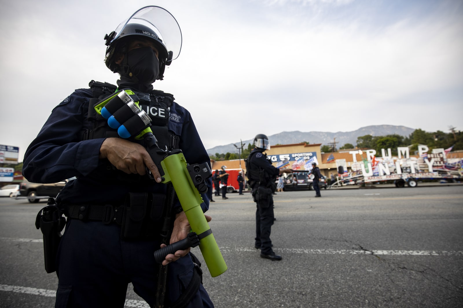 an officer in riot gear holds a less-lethal rifle