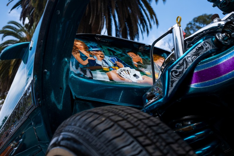 An illustration of men playing cards displayed on a lowrider.