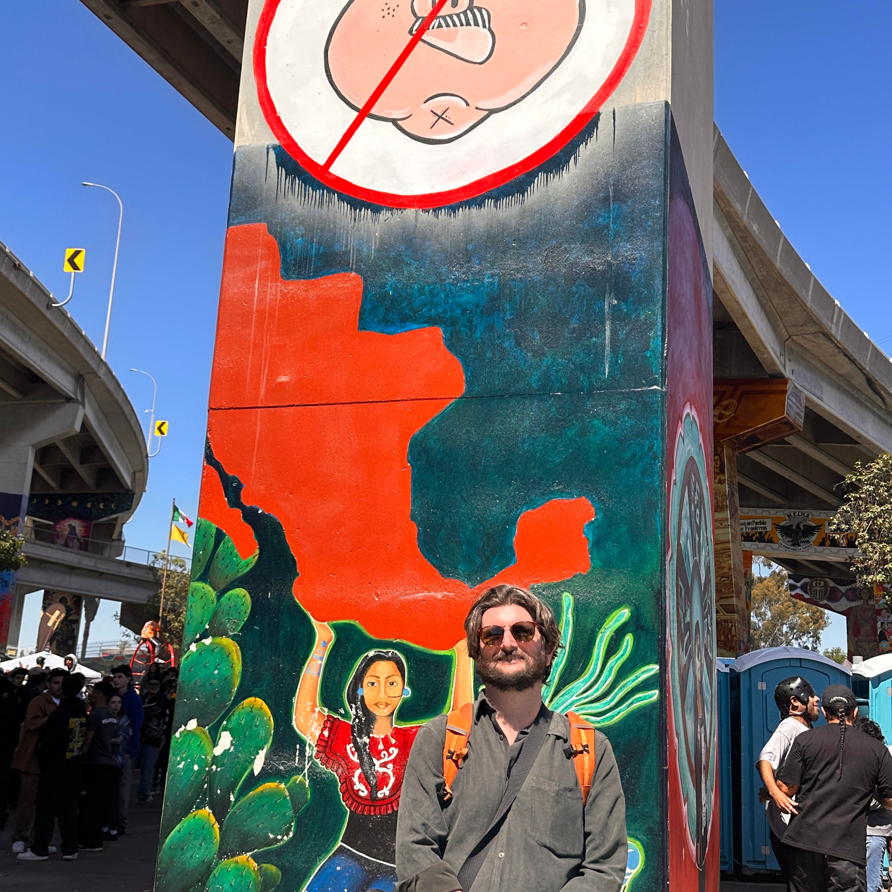 a man stands in front of a mural with a pig in a police hat being crossed out