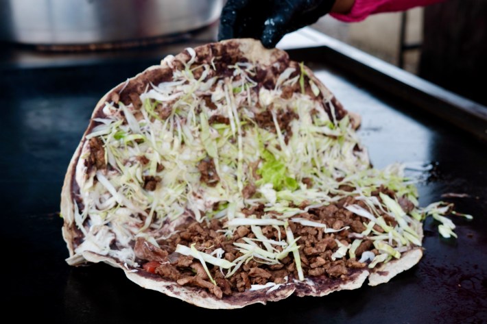 A tlayuda half-open and showing cheese, cabbage, and meat from Tacos Oaxaca in Los Angeles