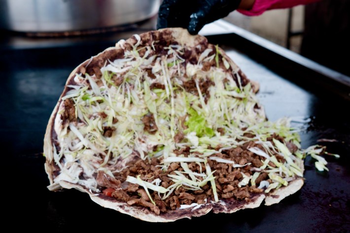 A tlayuda half-open and showing cheese, cabbage, and meat from Tacos Oaxaca in Los Angeles