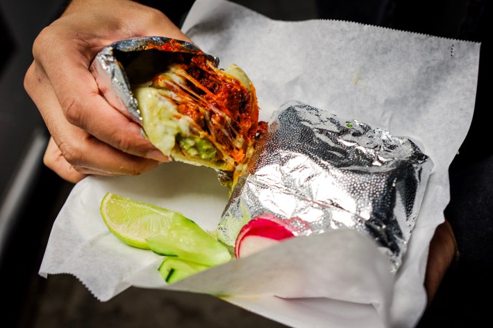 A burrito being split from its foil packaging with strings of cheese and red meat and salsa