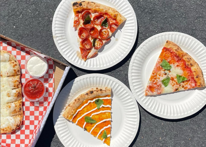 Three different slices of pizza on paper plates beside a French bread pizza at Echo Park's Naughty Pie Nature