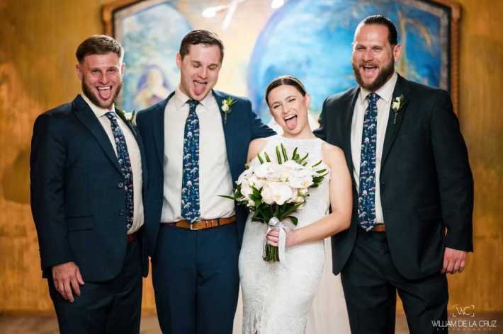 Jason Alex, Erika, and Michael Maccani stand together with big smiles on their faces, at Erika's wedding. Jason, Alex and Erika are all sticking out their tongues.