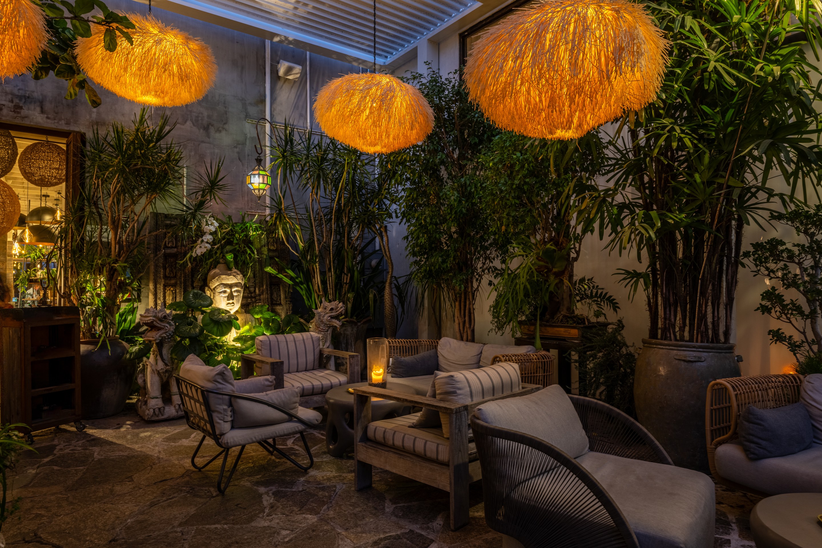 An outdoor area of The Woods dispensary and consumption lounge, showing lit up chandeliers, Buddha heads, and chaise lounges