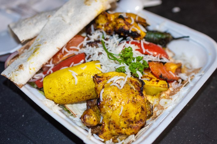 A takeout container full of Persian chicken kebab with rice and vegetables