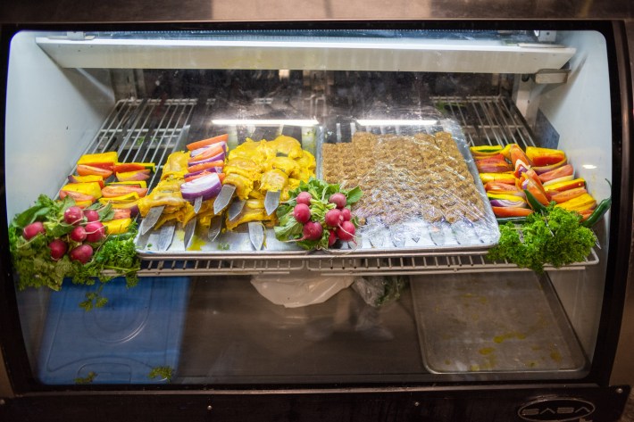 A look inside a streetside kebab display case, with skewered chicken, vegetables, and koobideh