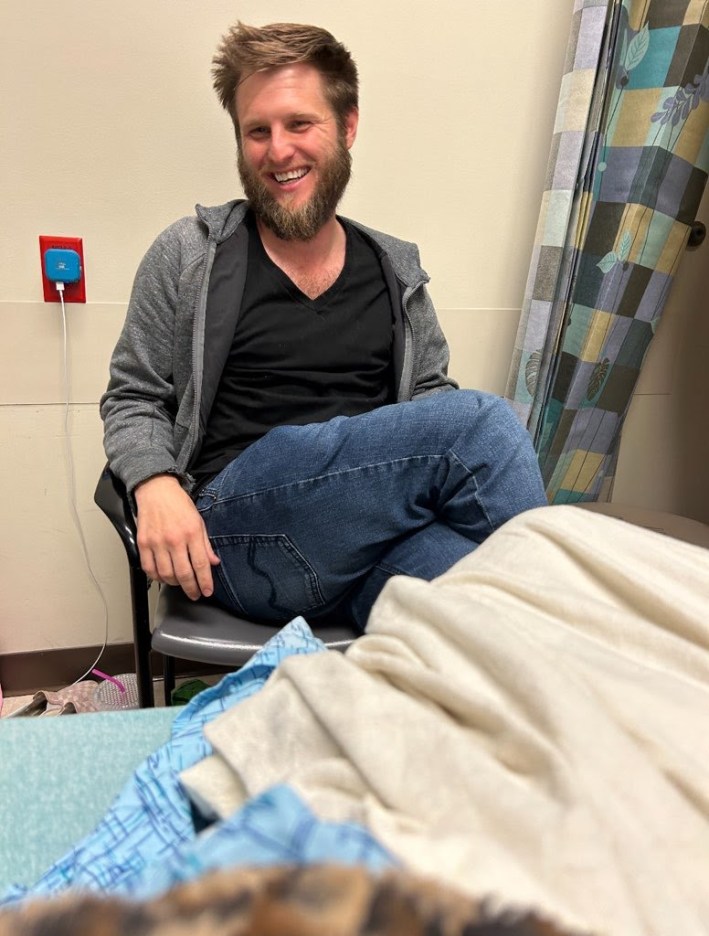 Jason Maccani sits in a chair while visiting his spouse at the hospital.
