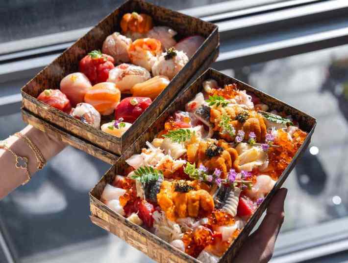 Two boxes of colorful raw fish topped with edible flowers in bento boxes from Wafu Bento