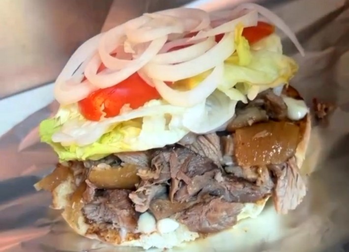 A breakfast torta stacked with carnitas, onions, lettuce, and tomato