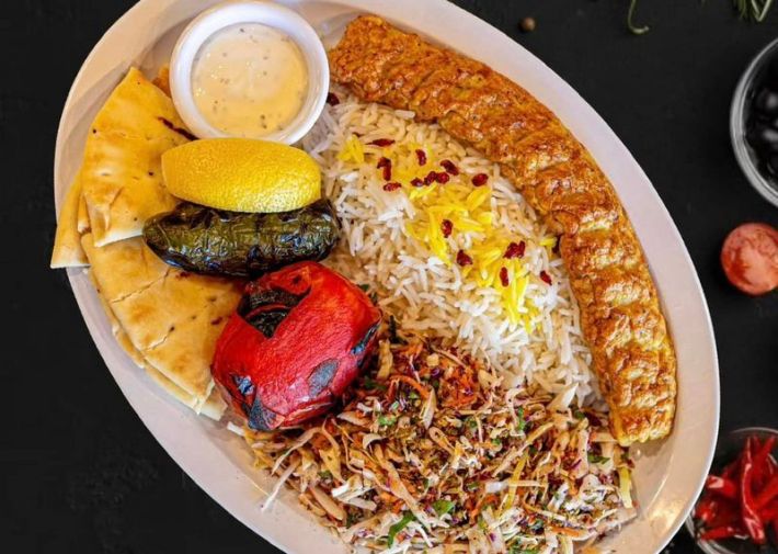 A plate of fish koobideh with rice, pita, and charred vegetables