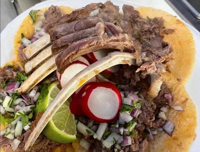 A rack of goat ribs atop a few birria de chivo tacos