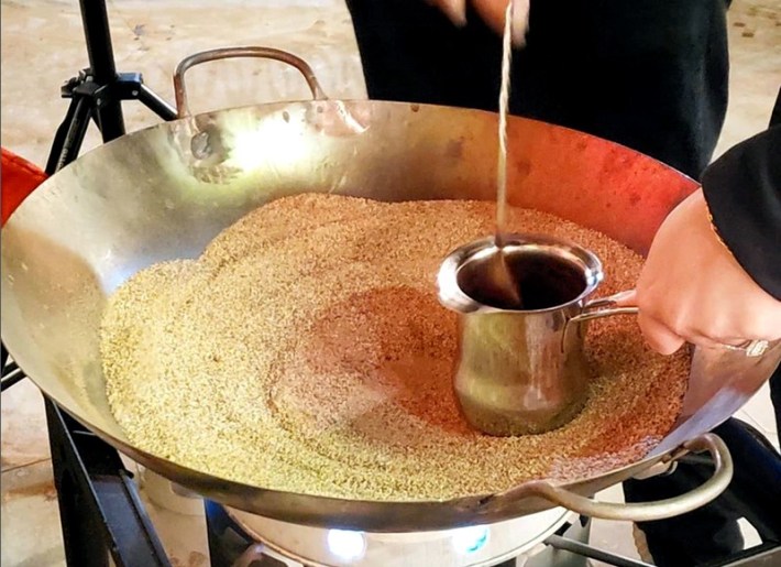 A pot of coffee being stirred in a large platter of hot sand