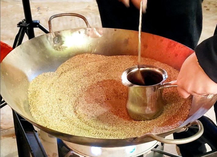 A pot of coffee being stirred in a large platter of hot sand