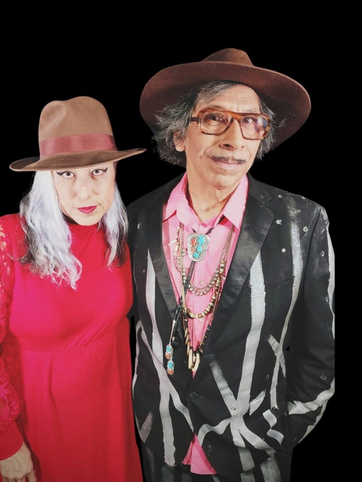 Alice Bag in a red dress and brown fedora next to Kid Congo Powers in a brown fedora and black suit painted with white designs