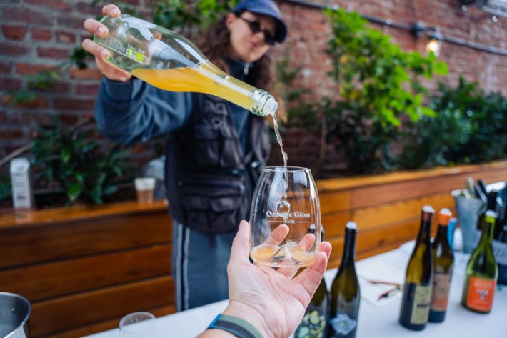 A woman pouring orange wine into a glass from an upturned bottle