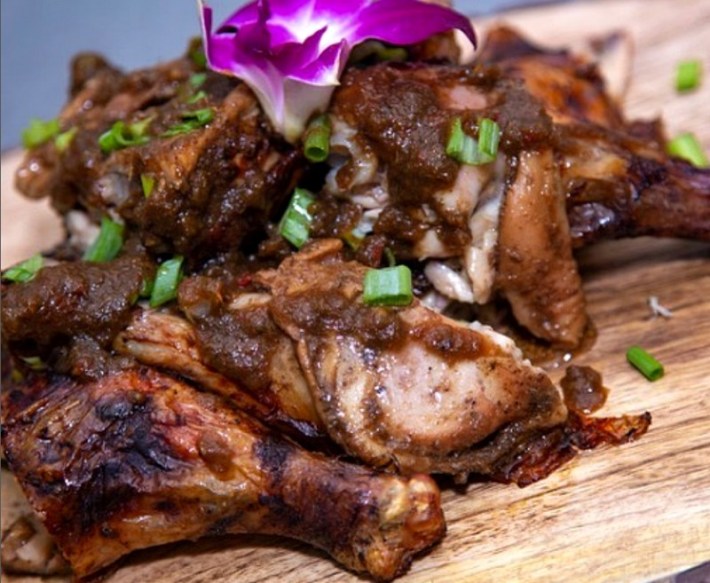 a small pile of jerk chicken crowned with a purple flower
