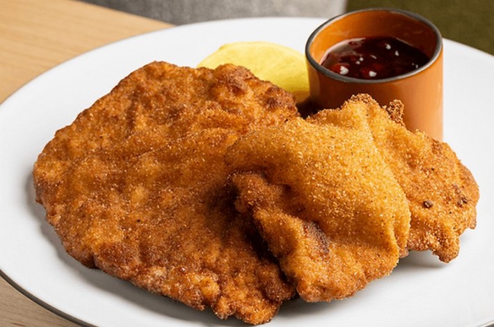 A golden plate of schnitzel next to a small pot of lingonberry-yuzu chutney