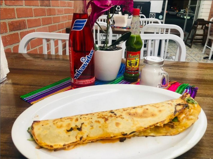 A long Guatemalan quesadilla on a white plate in a restaurant with a soda and salsa on the table