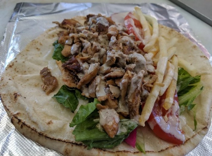 Pita spread with chicken shawarma, fries, onions, and tomato