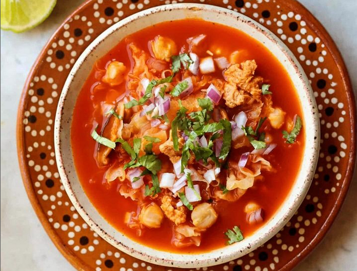 A red bowl of menudo with garbanzo beans