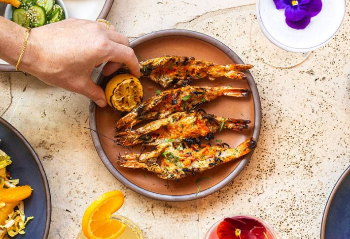 Two large split shrimp with a hand picking up a lemon from the plate.