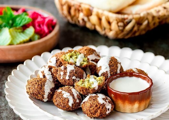 A paper plate of falafel balls drizzled in tahini sauce.