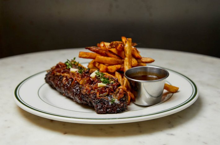 A white plate with steak frites and a cup of ketchup