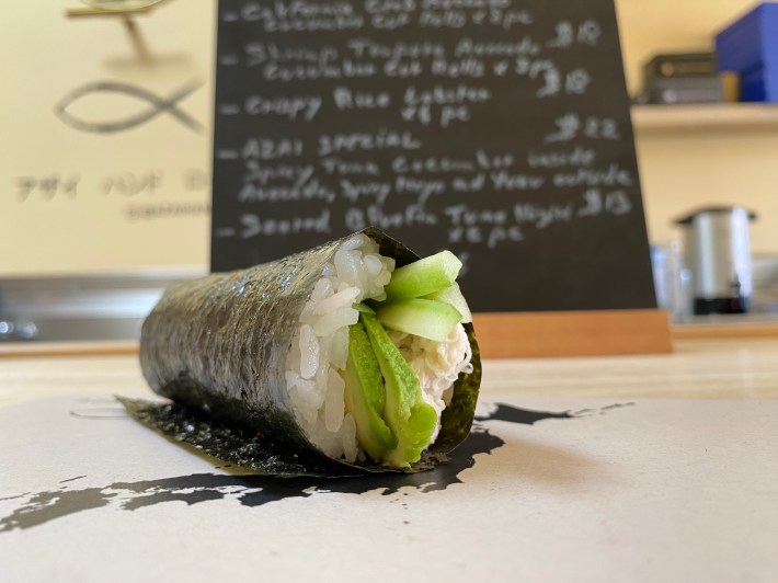 A hand roll with avocado coming out of the front