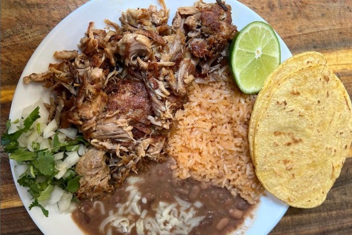 A plate of shredded carnitas with rice, beans, and two corn tortillas.