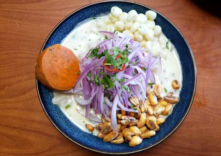 A plate of Peruvian ceviche with dried and fresh corn, red onions, and a sweet potato