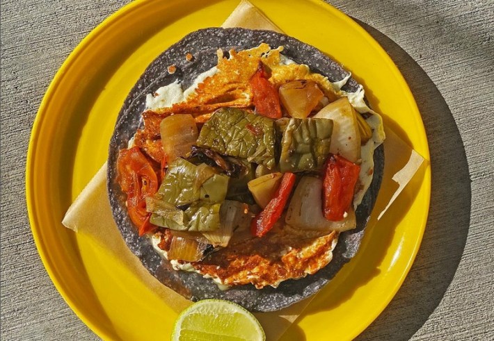 An open taco with fried cheese and vegetables on a blue corn tortilla.