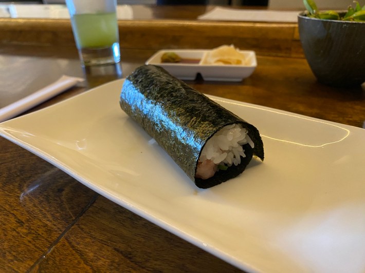 A closed hand roll with rice poking from out of the nori