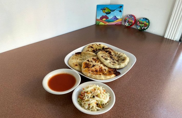 A plate of four pupusas on a table next to curtido and red salsa.