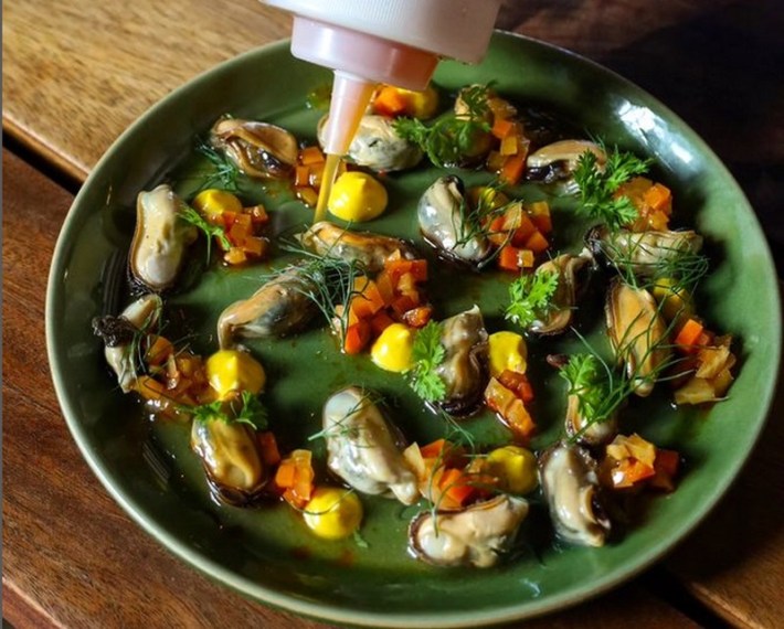 A plate of mussel escabeche with colorful dots of yellow aioli