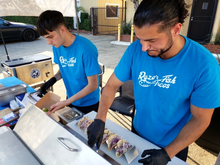 Two men in blue shirts plating fish tacos in North Hollywood