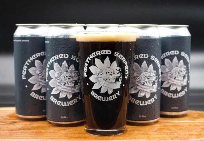 A pint of dark beer before four cans of beer from Feathered Serpent Brewery