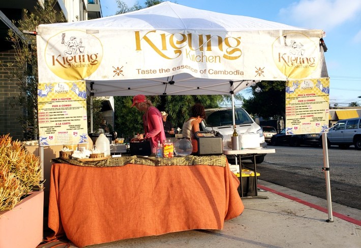 Kreung Kitchen's tent, with two employees making plates of barbecue