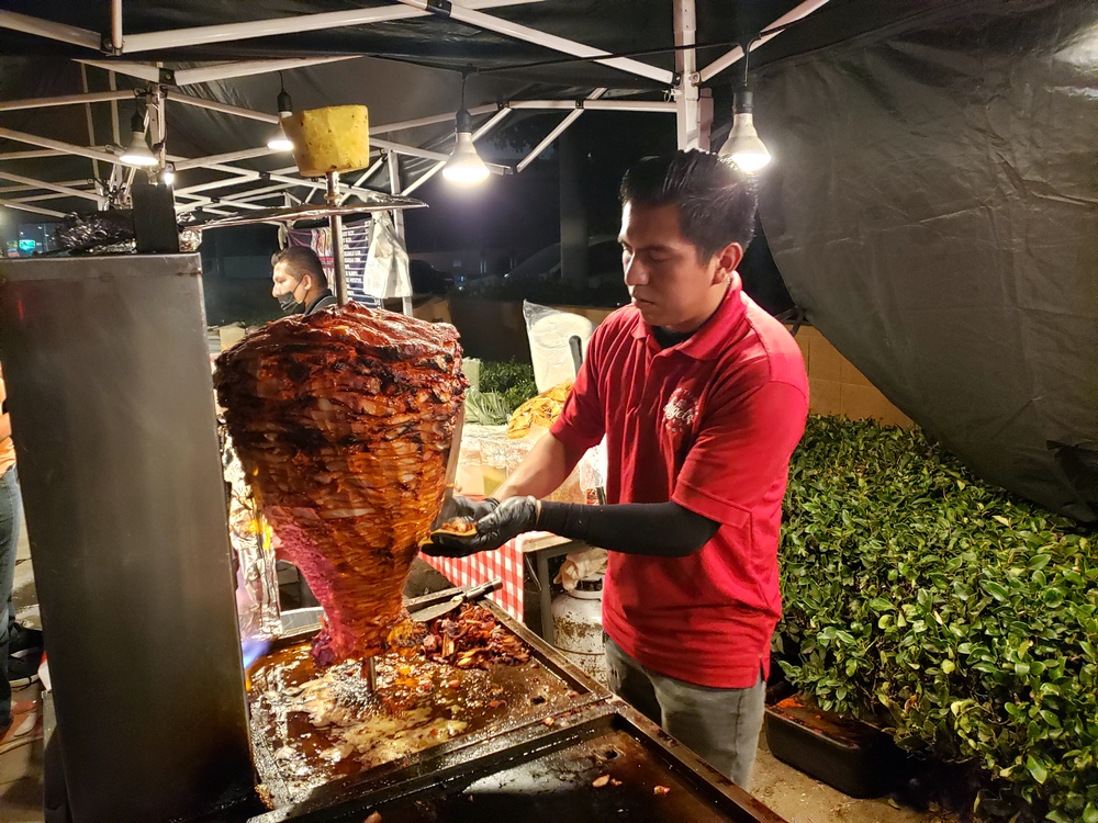 A skilled taquero in a red shirt carving a trompo of al pastor at Angel's Tijuana Tacos.