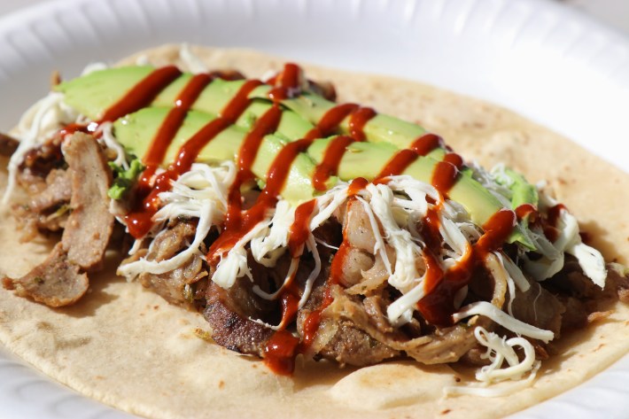 a taco with meat, cheese, avocado, and salsa on a flour tortilla