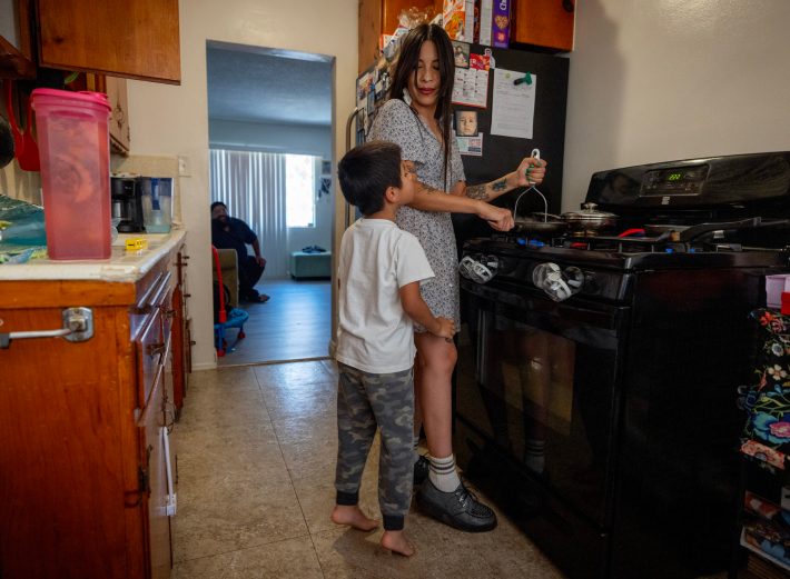 Wolfgang smells his lunch cooking while his Mom, Belen, prepares it in their East LA apt. Sept. 05, 2024. Belen Hernandez hit rock bottom in her early 30s. Down and out in the Boyle Heights neighborhood of Los Angeles, Hernandez and her partner, Henry Verdin, both drug addicts, were living hand to mouth when they were located by a family member, Salvador “Chava”Thomas under a bridge where they were staying. It was 2017. At the suggestion of a friend whose job involved finding housing for unsheltered people, Hernandez got in touch with the Los Angeles office of LIFT, a national nonprofit whose approach to elevating families out of low-income subsistence cycles looks and feels different. At LIFT, Hernandez was paired with a life coach and taught the basics of building financial stability. Even while trying to stay afloat from week to week, she was encouraged to think and talk about longer-term goals – and to speak some of those dreams aloud. After a couple of years of mentorship and stabilizing her family’s finances, she participated in a LIFT-organized community business academy to learn how to create and run a small company. Today, Hernandez and Verdin, now her fiancé, remain in the film production security business – only now they are the owners of their firm, rather than hourly workers. Photo by Barbara Davidson / Capital and Main