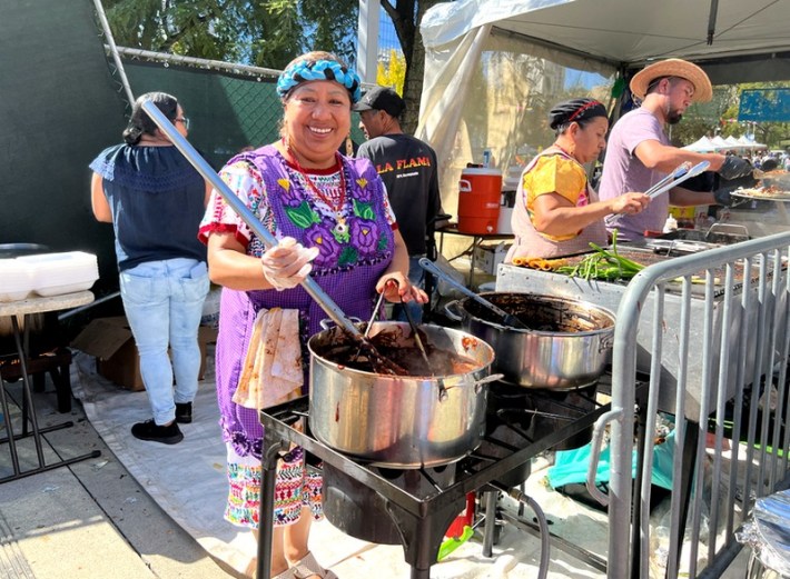 A female chef makes mole in a big pot while wearing traditional Oaxacan outfit at La Feria de Los Moles