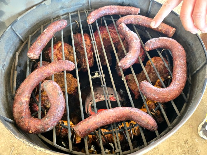 A layer of morcilla (blood sausages) smoking over chicharrones, hung by hooks on the side of the barril