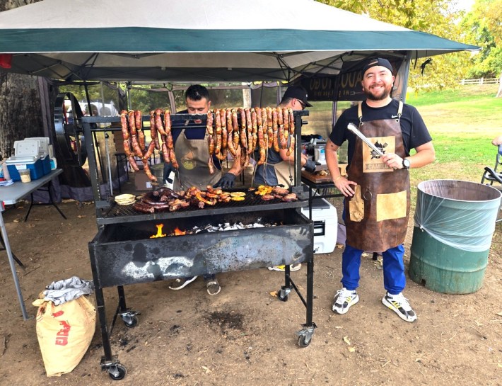 Camilo Valero standing next to the grill full of meats at Asado To Go.