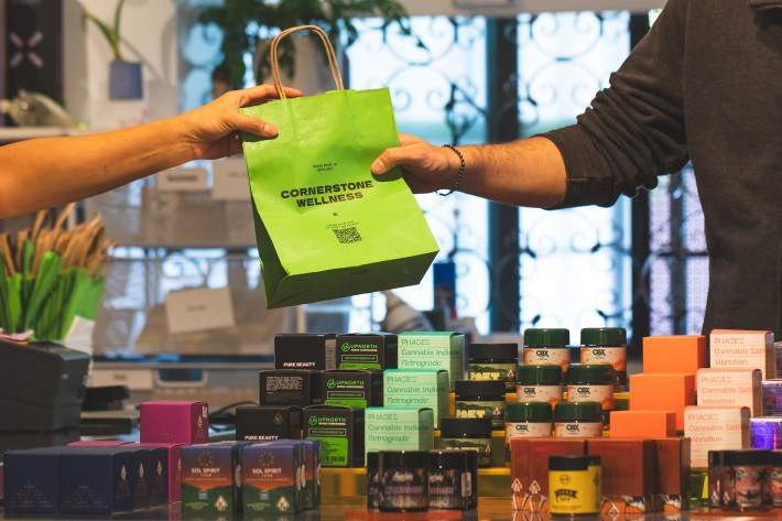 A green bag being passed from one hand to another at Cornerstone Wellness dispensary